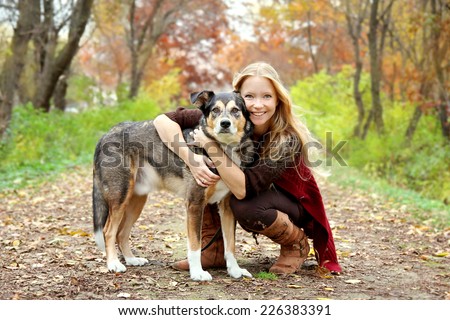 A thirty year old woman is stopping to hug her German Shepherd dog as they are walking through the fallen leaves in the woods on an Autumn day.