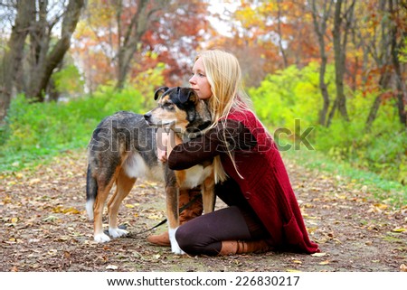 A young woman and her German Shepherd dog have stopped on a walking trail in the woods to look at something and relax on an autumn day.