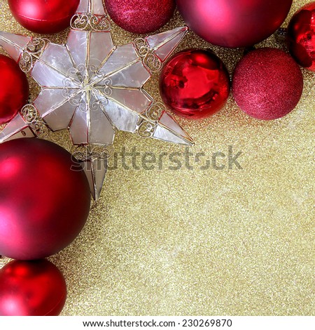 Red Christmas bulb decorations and a star shaped tree ornament border the corner of a background gold glitter fabric with copy-space.