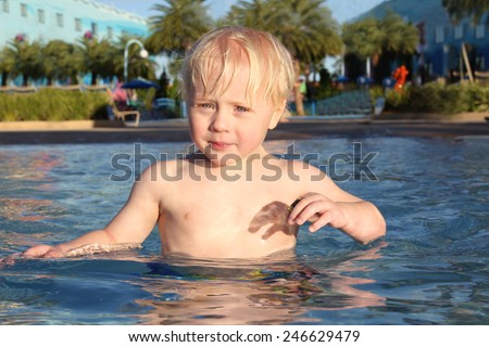 A young child is wading in the zero entry zone of a swimming pool on a summer day.