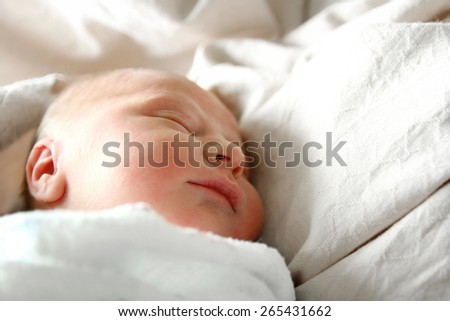 A one day old newborn baby is sleeping swaddled in white blankets in her hospital bed.