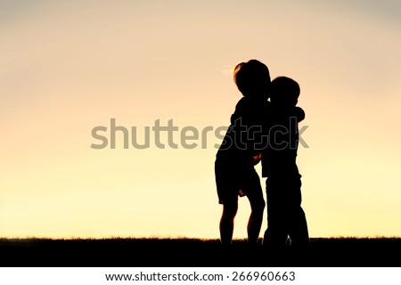 A silhouette of two little boys, a young child and his toddler brother, hugging at sunset.