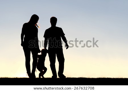 A silhouette of a family of three people, including mother, father, and young child are playing around while walking outside at sunset.