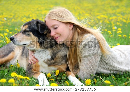 A girl is laying outside in the grass, tenderly hugging her aging German Shepherd mix dog with her eyes closed.