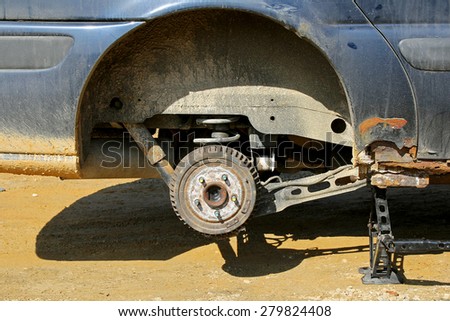 An old rusty automobile is lifted up on a jack with the wheel removed to change the tire.