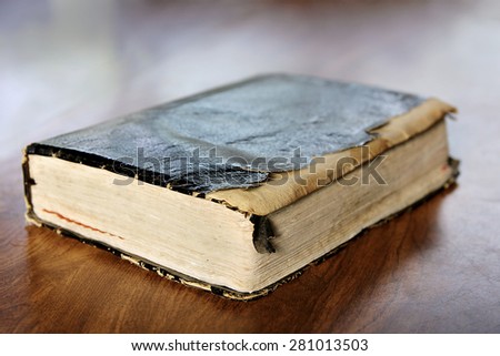 Close up on a black leather bound tattered and torn old vintage book, the Holy Bible sitting on Wooden Table.  Shallow depth of field.