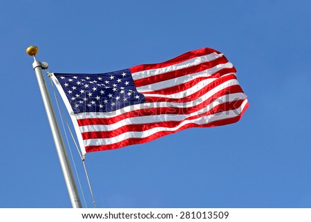 A red, white and blue American Flag is raised into the blue sky, blowing in the wind.