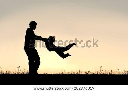 Silhouette of a happy father holding his little child\'s arms and spinning him in circles on a summer day.