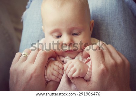 Close up on a newborn baby girl\'s hands holding the fingers of her father as she sits on his lap at home. Vintage style color filter.