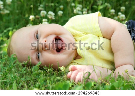 A chubby and happy newborn baby girl is laughing as she lays outside in the grass in a flower meadow