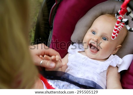 A beautiful newborn baby girl is laughing and sticking out her tongue as her mother holds her hands while she sits in her car seat.