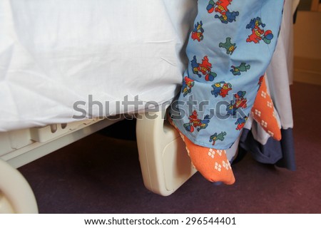The feet of a young child wearing scrub pajamas are resting on a hospital bed.