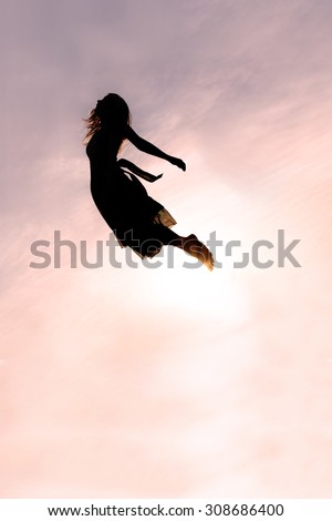 Silhouette of a young woman falling head-first through the sky at sunset.