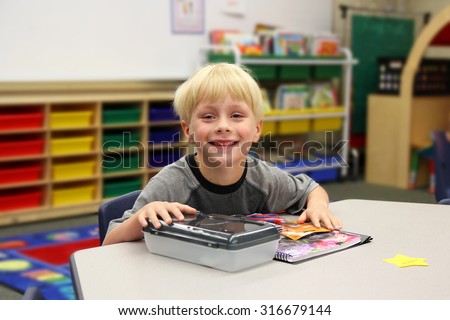 A young boy is sitting at his desk on his first day of school in his kindergarten classroom.