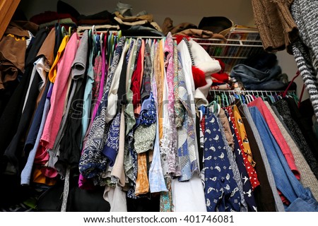 A messy young women's closet is fill with many outfits of colorful clothing, shirts, and dresses.