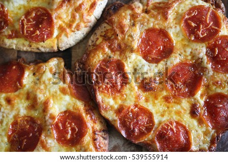 A group of small, personal pan, handmade fresh pepperoni pizzas are sitting on a wooden table.