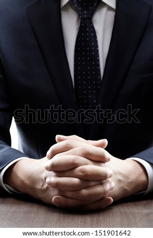 close up of a man in a suit with his hands clasped in front of h
