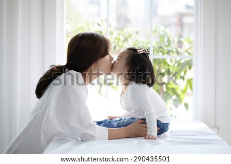 beautiful Asian mom and her cute daughter kissing with love while looking at each other