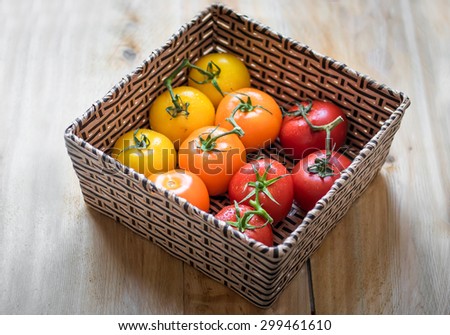 10 tomatoes of different color red, orange and yellow inside a square basket on top a wood table.