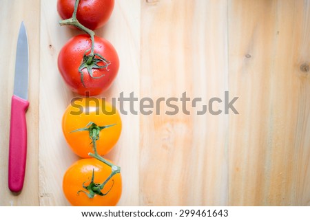 Four fresh tomatoes in different colors, red and orange in line form on top of a light wood table.