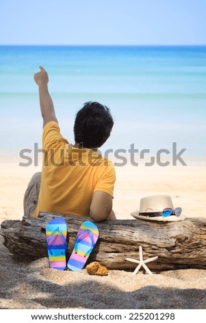 a man sitting on the beach with hat over old log and slippers