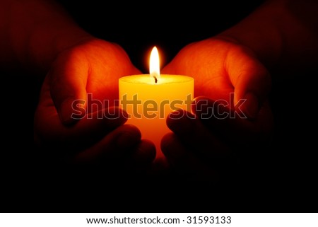 Heart-shaped hands holding yellow candle in dark