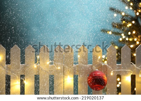 Christmas ball and lights hanging on fence at snowy night