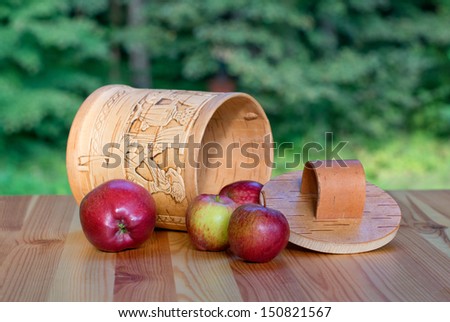 birch bark box and apples on wooden table  against background blurred foliage