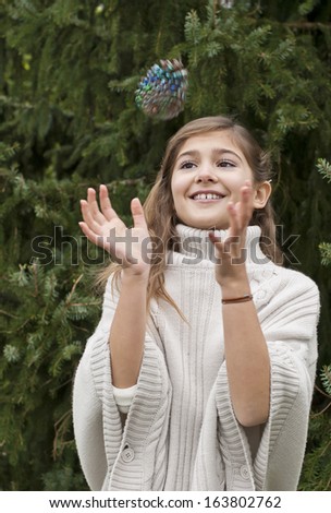 Young pretty girl throwing and catching a pine cone near a fire tree outside