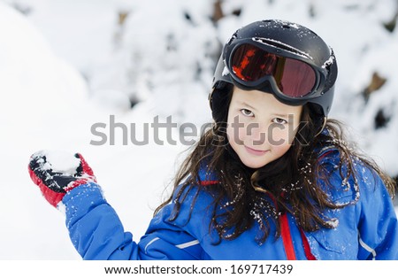 Pretty young girl wearing a ski helmet and holding a snowball