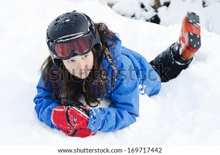 Pretty young girl laying in the snow wearing a ski helmet