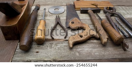 Old hand tools in a row. Old rusty and dirty carpenter`s hand tools lying in a row on wooden table.