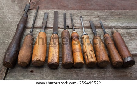 Carpenter tools row. Old carpenter chisels, screw driver, file & awl laying on dirty wooden table angle view.