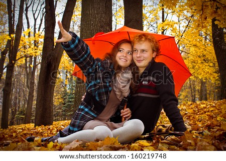Young happy couple sitting under the orange umbrella in the park enjoying sounds of nature