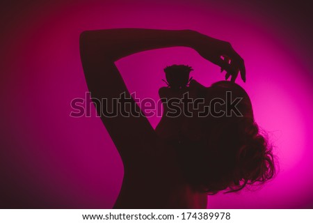 Silhouette of young beautiful girl hiding red rose in mouth