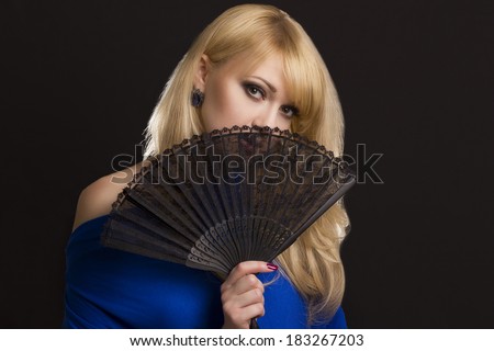 Beautiful young woman with a fan in hands on black background