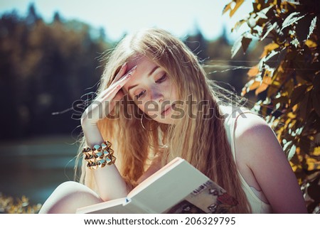 Beautiful young girl with long hair reading a book on nature