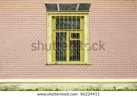 Yellow window with bars on a painted brick wall