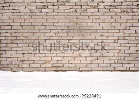 Old wall of white bricks and a ground covered with snow