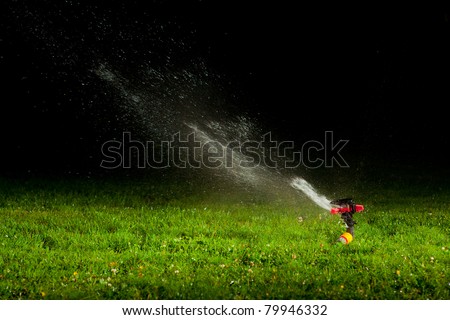 lawn sprinkler spraying water over green grass at night