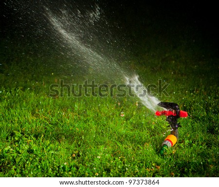 lawn sprinkler spraying water over green grass at night
