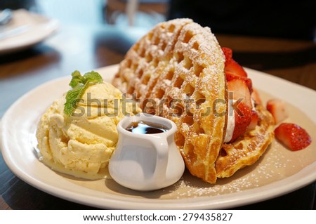 Plate of waffles with ice cream, caramel sauce and fresh strawberries.