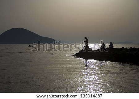 Fishing men on rocks and in boat during sunset
