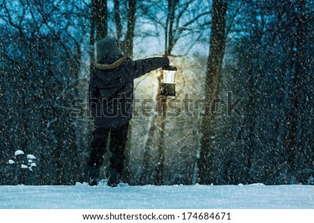 a snowy scene of a boy holding a lantern and peering into the the woods
