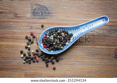 asian spoon filled with gourmet peppercorns against a wooden background