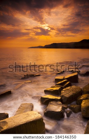 Waves wash over the rocks at Kimmeridge in Dorset on the Jurassic Coastline. The golden-hour sunset causes yellow, white and gold reflections on the wet rocks