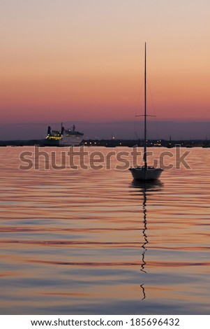 Yacht silhouetted against a pink and purple sky on calm seas inside Poole harbor with the cross-channel ferry in the distance