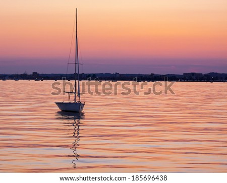 Yacht silhouetted against a pink and purple sky on calm seas inside Poole harbor