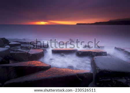 The sun sets on the beautiful Dorset coastline illuminating glistening rocks with orange and yellow highlights