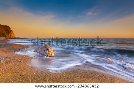 The sun sets illuminating the wet rocks and pebble beaches of the Jurassic Coast